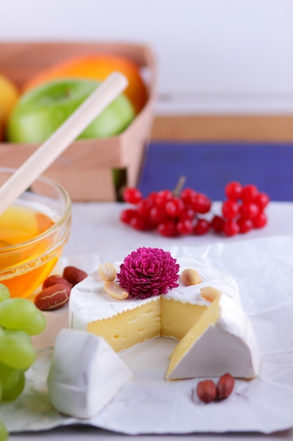 Gourmet white brie or camembert cheese with berries honey and nuts on a white background Still life of cheese honey walnuts and grapes Closeup