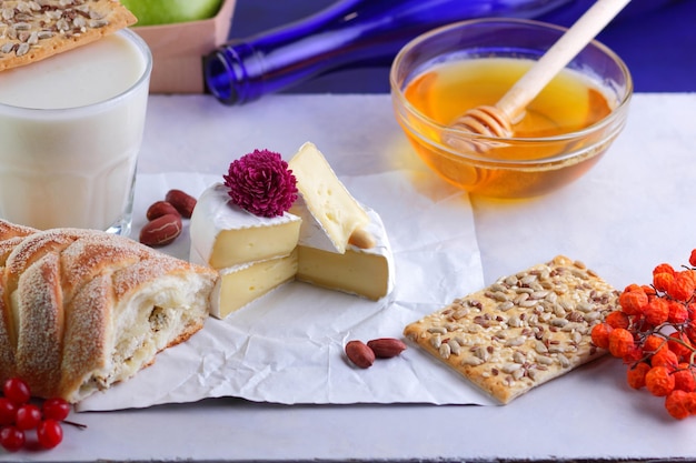 Gourmet white brie or camembert cheese with berries honey and nuts on a white parchment Still life of cheese fruit and a blue bottle on a blurred background Closeup