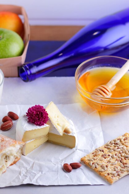 Gourmet white brie or camembert cheese with berries honey and nuts on a white parchment Still life of cheese fruit and a blue bottle on a blurred background Closeup