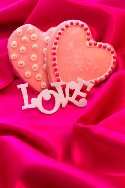 Gourtmet heart shaped cookies decorated for Valentine's Day on pink silk.