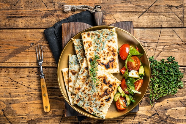 Gozleme flatbread with greens and vegetable salad on garnish Wooden background Top view