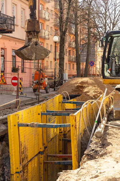 Foto graafmachine die diepe uitgravingen vult, ondersteund door een geulbak met pijpbedding, erwtengrind tijdens de installatie van de afvoerleiding