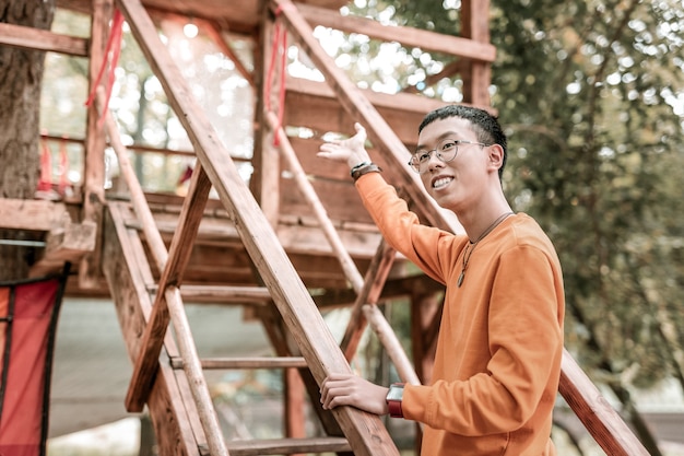 Graag gedaan. Positief opgetogen Aziatische man die een glimlach op zijn gezicht houdt en op de trap staat