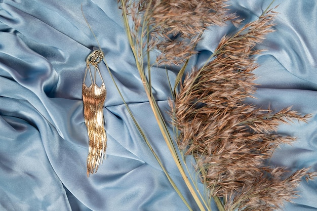 Graceful background with stylish golden earrings pampas grass and folded silk textile Cozy stilllife backdrop