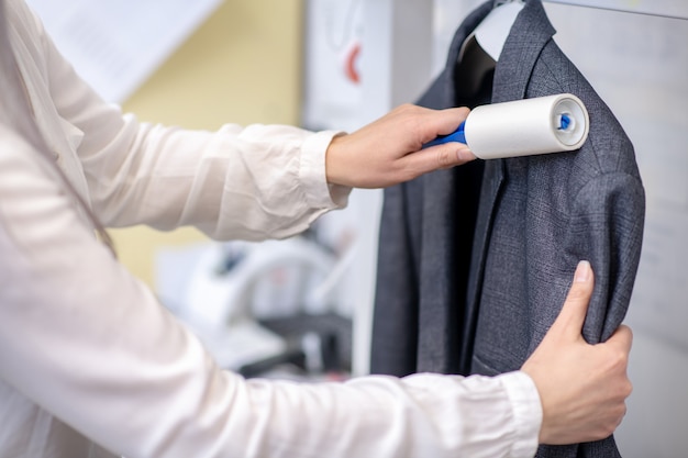 Graceful caring female hands cleaning jacket with roller, face is not visible