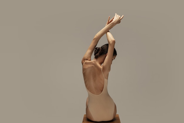 Graceful classic ballerina dancing, posing isolated on pastel brown studio background. Females back and hands. The grace, artist, movement, action and motion concept. Looks weightless, flexible.