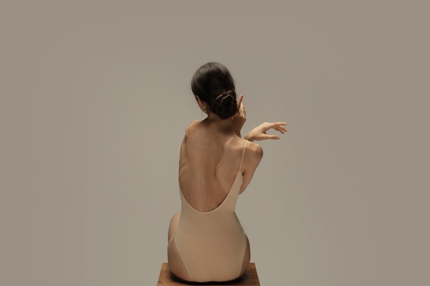 Photo graceful classic ballerina dancing, posing isolated on pastel brown studio background. females back and hands. the grace, artist, movement, action and motion concept. looks weightless, flexible.