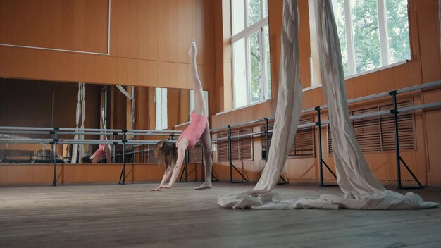 Foto graziosa ragazza in abito rosa e scarpe da punta ballerina che pratica in studio, elementi di danza, teleobiettivo