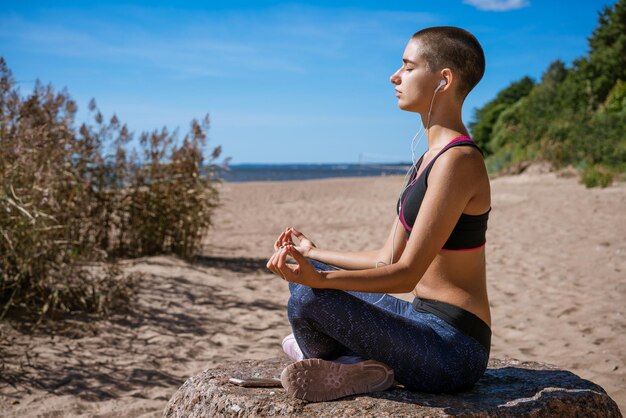 Graceful woman doing yoga asana on beach in headphones meditates on seashore