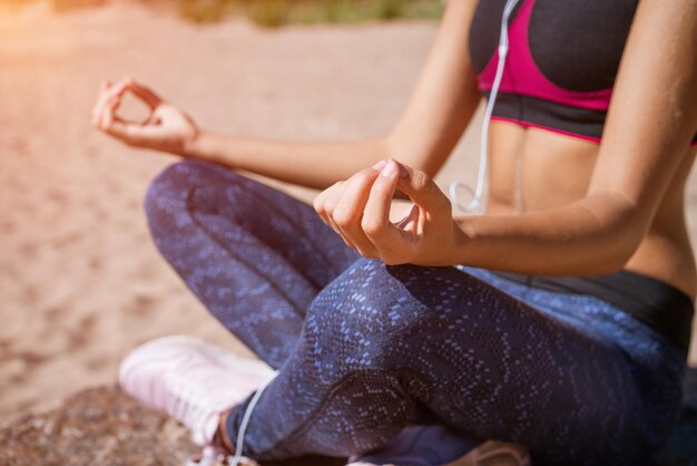 Donna graziosa che fa yoga asana sulla spiaggia in cuffie medita in riva al mare