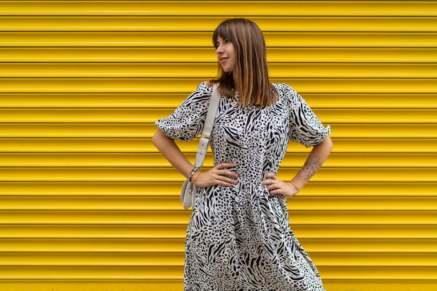 Graceful woman with tatoo on hand posing over yellow  urban wall.