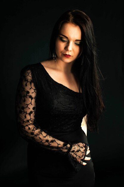 Graceful young woman in black dress against dark background