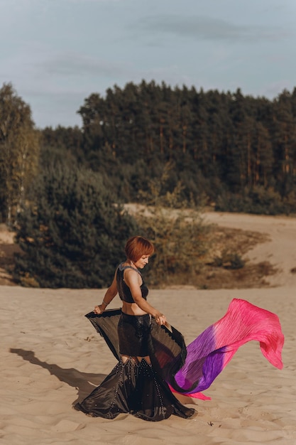 Gracieuze vrouw in buikdans kostuum dansen op het zand bij zonsondergang