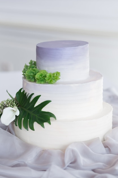꽃과 녹색 야자수 잎이 있는 흰색 웨딩 다단계 케이크가 있는 그라데이션 라일락