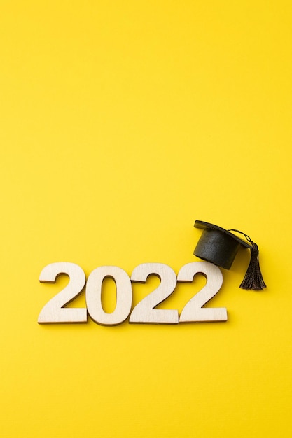 Фото Шляпа выпускника с деревянным номером 2022 на желтом фоне. образование, обучение, концепция класса 2022 вертикальный формат