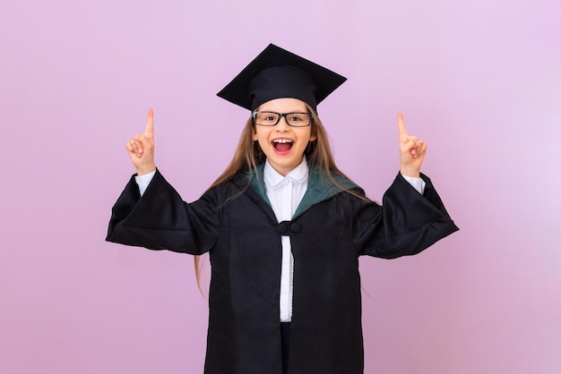 A graduate in a black robe and a square cap points her fingers up at the advertisement and smiles. isolated background.