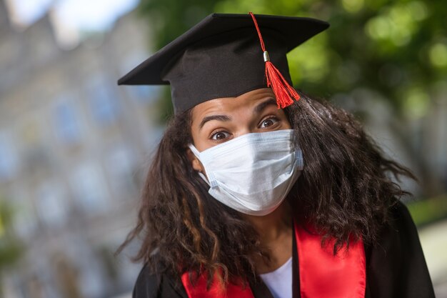 Laureato. una ragazza carina dalla pelle scura con un berretto accademico e una maschera preventiva