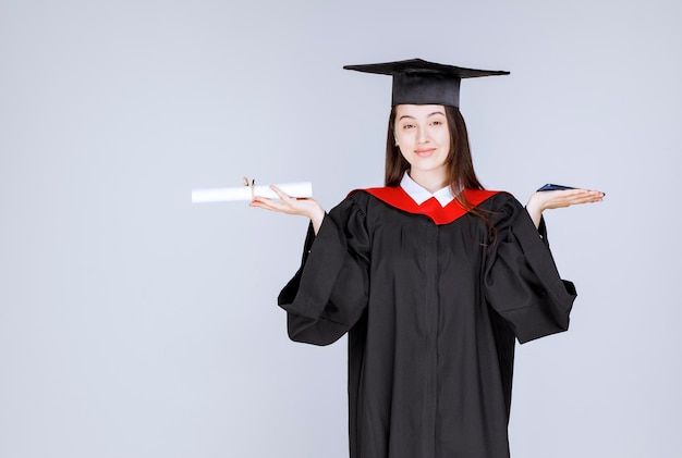 Graduate student in gown holding cellphone and diploma. High quality photo