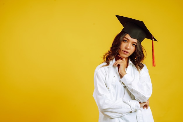 Graduate woman in a graduation hat on her head posing on yellow