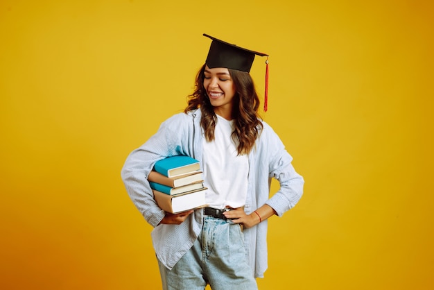 Graduate woman in a graduation hat on her head, with books on yellow