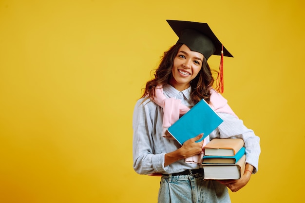 Foto donna laureata in un cappello di laurea in testa, con libri su giallo.