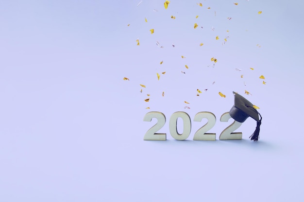 Graduation 2022 wearing a graduate hat on a wooden 2022 number on a very threaded colored background with flying confetti