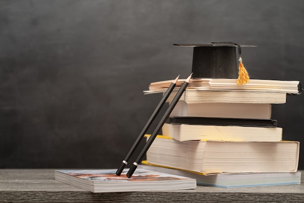 Foto tappo di laurea, libri e matite sulla scrivania