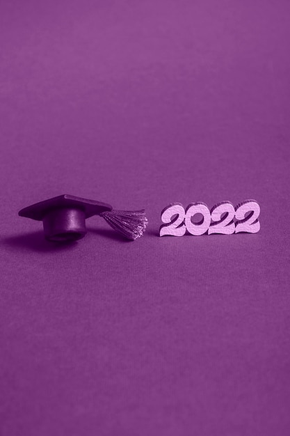 Graduation cap  and numbers 2022 on violet background, close up with copy space. Medical education concept. Vertical format