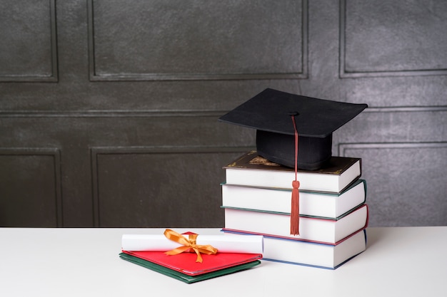 Foto protezione di graduazione con i libri sullo scrittorio bianco, fondo di istruzione