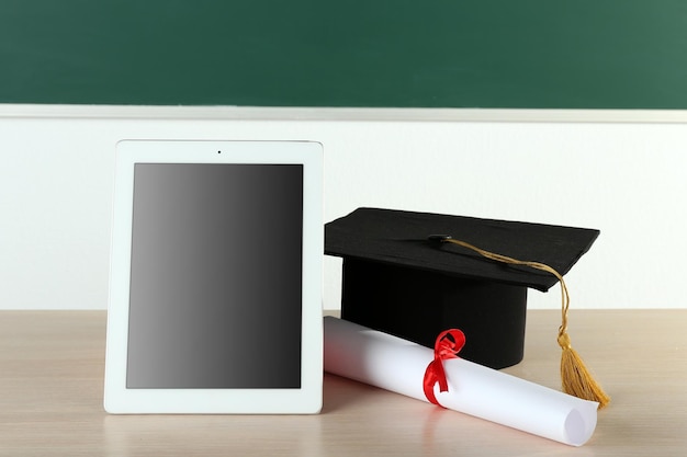 Photo graduation cap with tablet and diploma on table in class