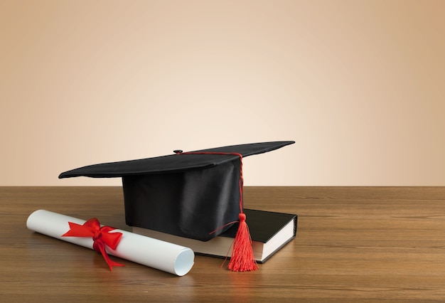 Graduation hat, book and diploma on wooden table