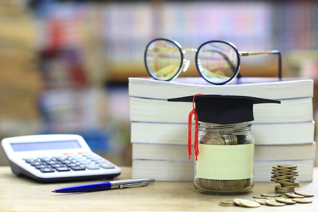 Cappello di graduazione sulla bottiglia di vetro sullo scaffale per libri nella stanza della biblioteca, risparmiante i soldi per il concetto di istruzione