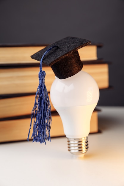 Фото Выпускной шляпа на лампочке с книгами на столе. вертикальное изображение. концепция образования.