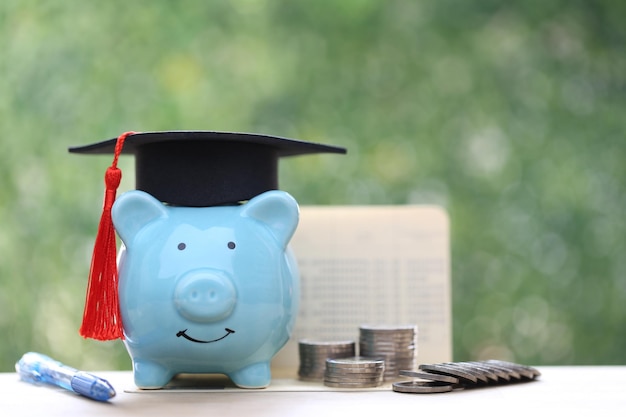 Cappello di graduazione sul salvadanaio con una pila di monete denaro su sfondo verde naturale risparmiare denaro per il concetto di istruzione