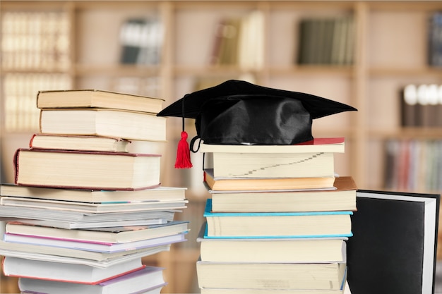 Graduation mortarboard on top of stack of books on  background