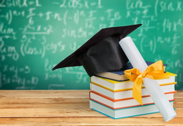 Graduation mortarboard on top of stack of books on  background