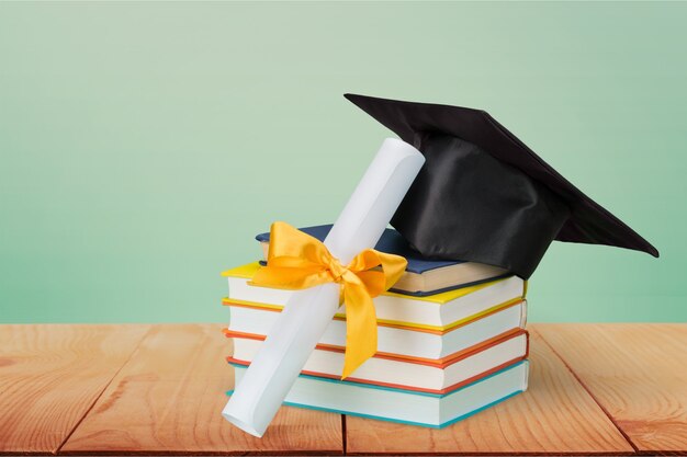 Graduation mortarboard on top of stack of books on  background