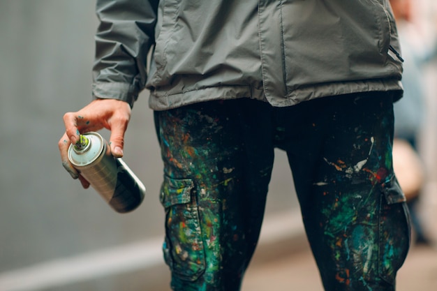 Graffiti artista in abiti macchiati con vernice spray in mano