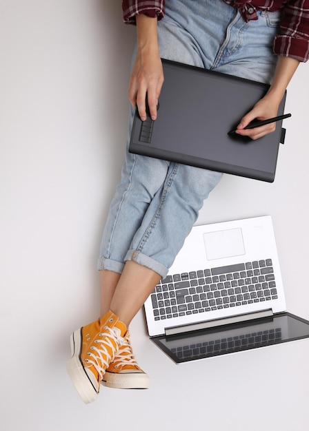 Grafisch ontwerper of fotograaf baan. Vrouw werkt met grafisch tablet en laptop zittend op een witte achtergrond. Freelance, online werkconcept. Bovenaanzicht