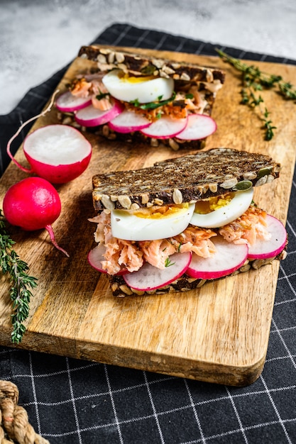 Grain bread sandwiches with hot smoked salmon, eggs and radishes. Healthy balanced food. Gray background, top view.