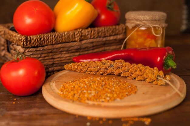 Grains and chili are on the plank near a basket with tomatos on the table