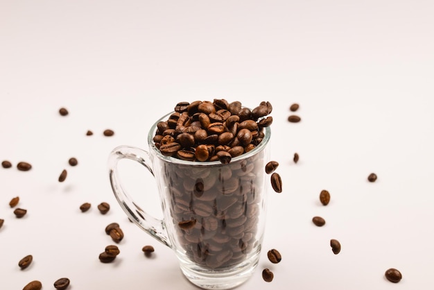 Grains of coffee are poured into a glass cup on a white background