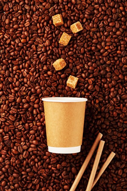 Grains of coffee drink and pieces of cane sugar in zero waste paper cup on grains background. Plastic free concept. Selective focus.