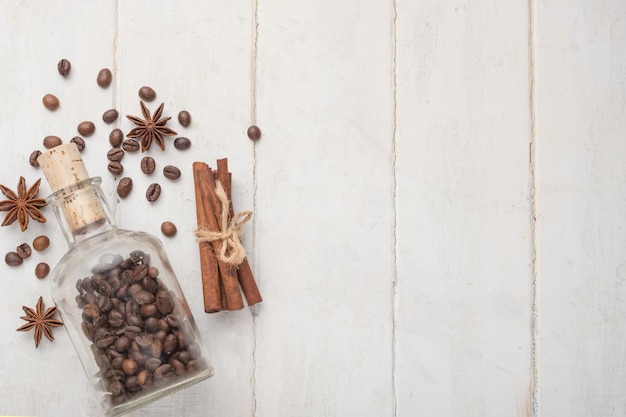 Photo grains of coffee in a glass jar with cinnamon and badan on a light wooden texture with empty space for writing