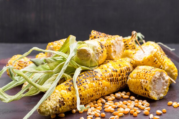 Grains of corn grilled corn with leaves. Copy space. Rusty and black background.