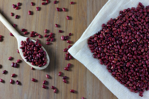 Grains red bean bag on side of wooden table, wooden spoon with red beans, top view