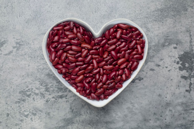 Зерна Красная фасоль в миске в форме сердца на бетонном фоне