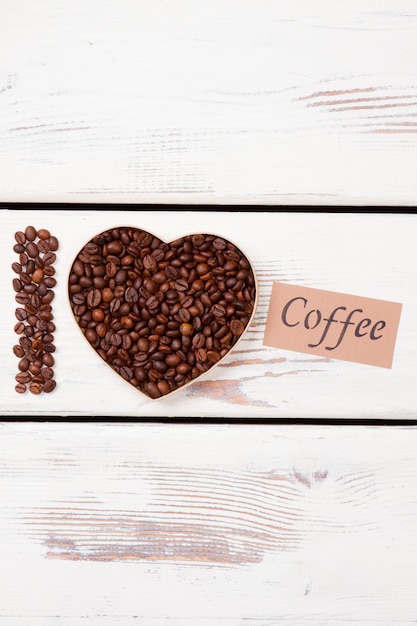 Grains roasted coffee in a shape of heart. I love coffee. White wood surface.