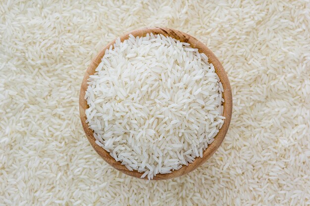 Зерна тайского жасминового риса в деревянной миске на фоне белого риса