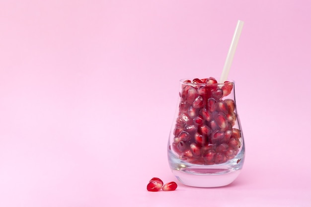 Granaatappelpitjes in het glas op de roze achtergrond. Gezond, biologisch productconcept. Kopieer ruimte.